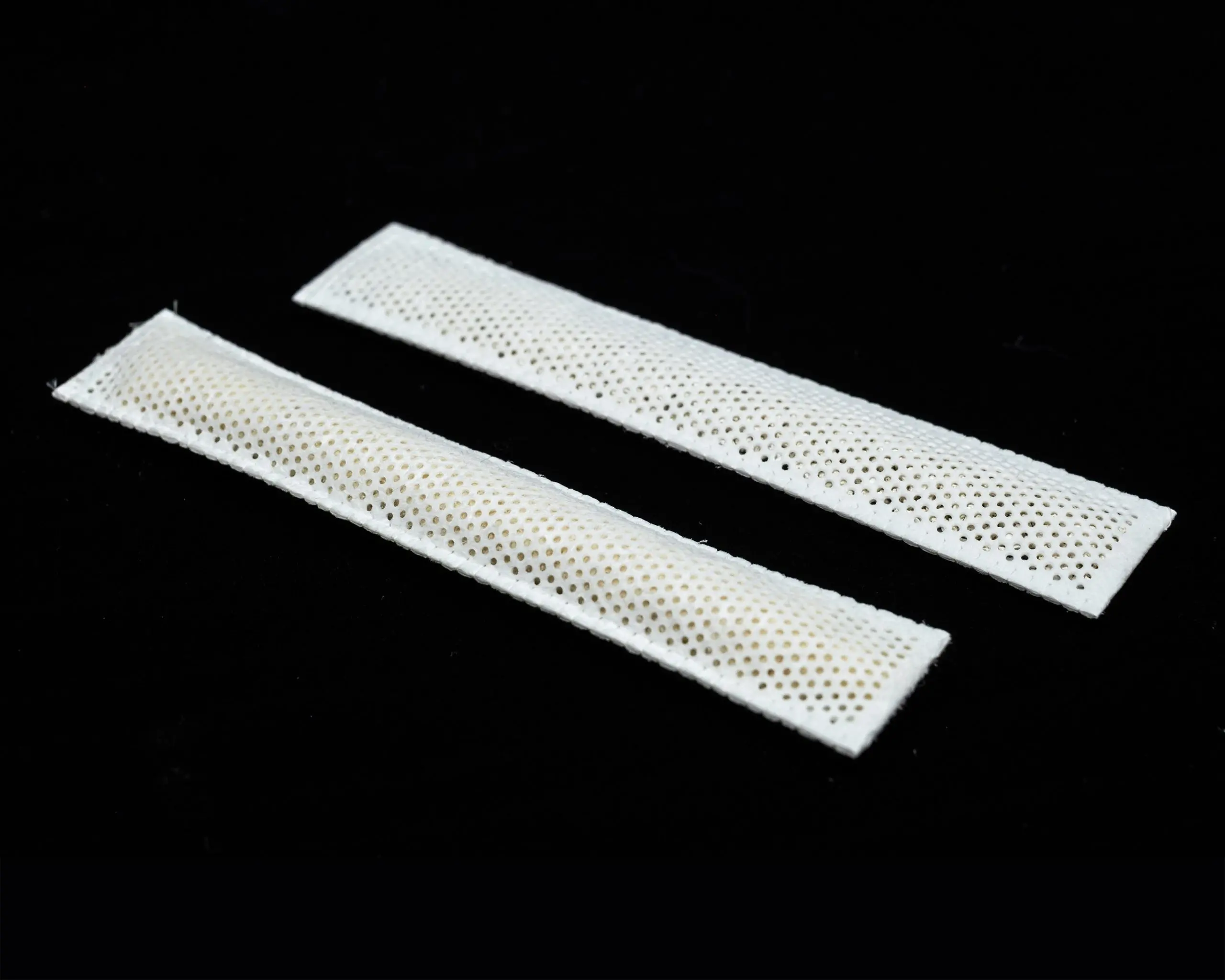 White perforated fabric strips laid diagonally on a black background, close up detail of the mesh pattern.
