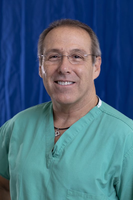 Smiling man in green scrubs with glasses, posed against a blue backdrop.
